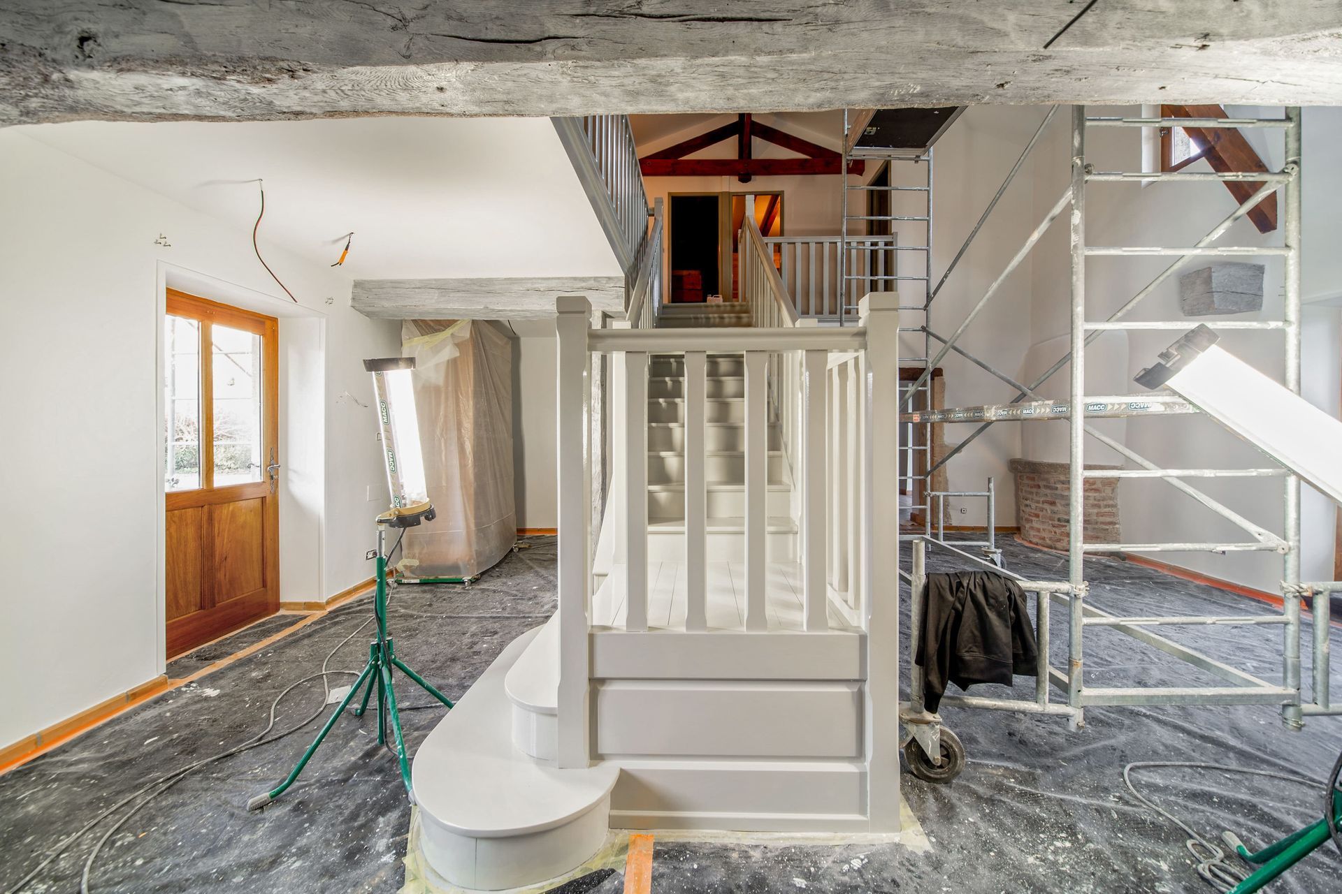 Chantier de rénovation avec échafaudages, plafond apparent et escalier blanc