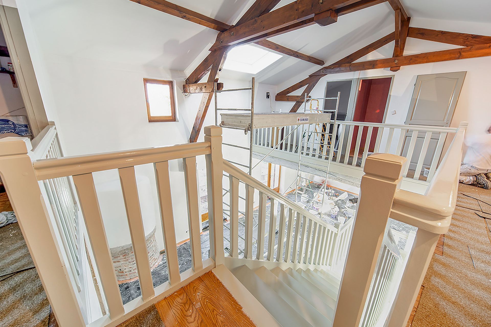 Couloir lumineux avec rampes blanches, poutres en bois et escalier donnant sur un niveau inférieur