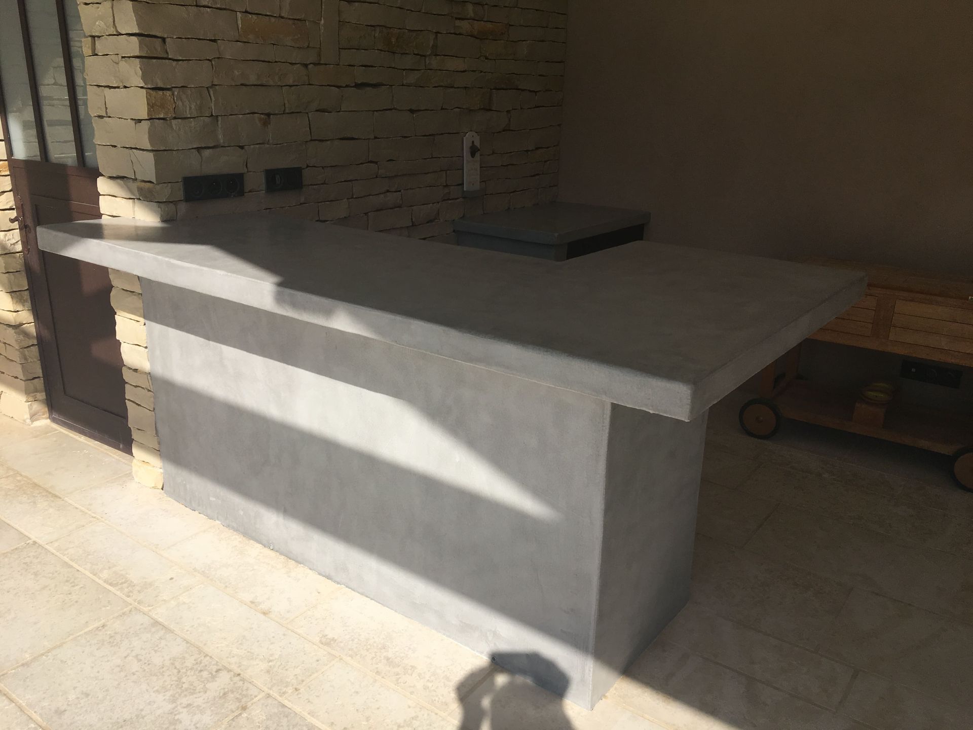 Comptoir en béton dans un patio ensoleillé avec un mur en briques et un sol carrelé