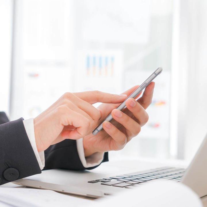 Des mains tapant sur un smartphone à côté d'un ordinateur portable dans un bureau lumineux