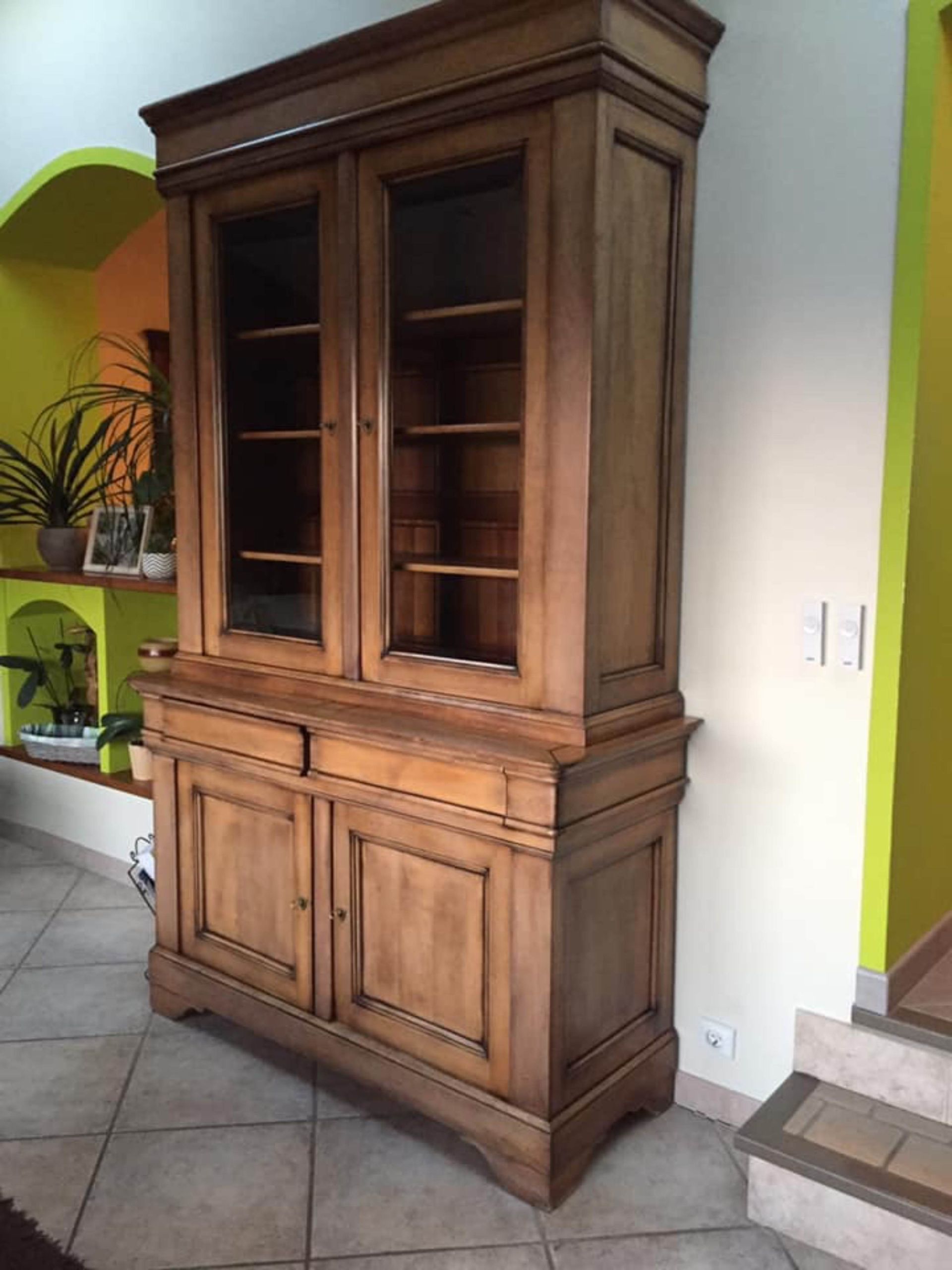 Armoire haute en bois avec portes vitrées et rangements inférieurs dans une pièce carrelée