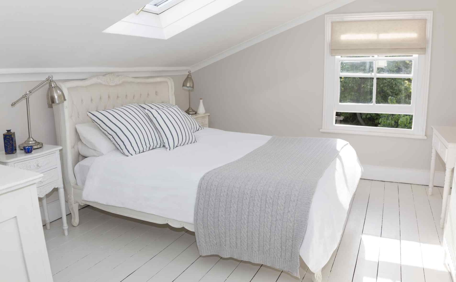 Chambre blanche lumineuse avec un lit, une table de chevet, un puits de lumière et une fenêtre.