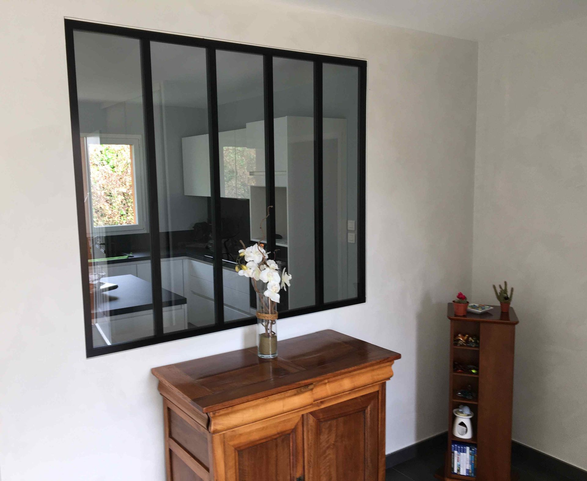 Meuble en bois avec vase sous un miroir mural à cadre noir dans une pièce lumineuse