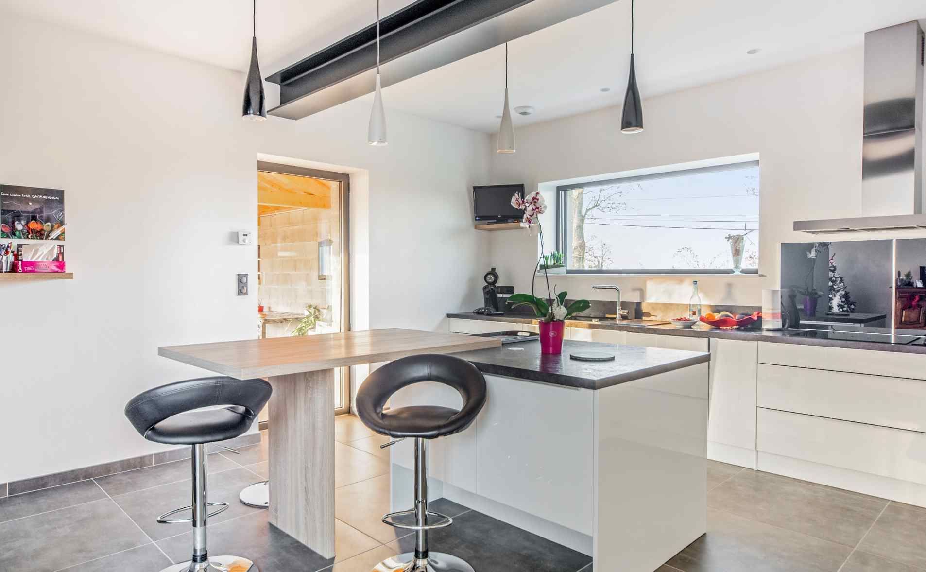 Cuisine moderne avec armoires blanches, îlot central, tabourets noirs, suspensions lumineuses