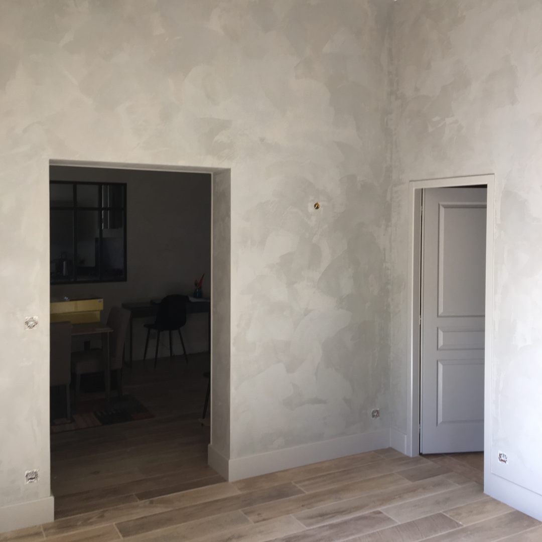 Pièce vide aux murs gris texturés, parquet clair, porte ouverte et porte blanche fermée