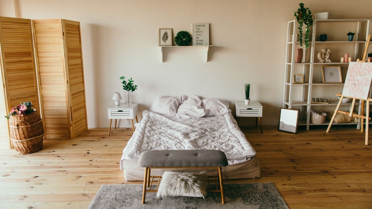 Chambre confortable avec un lit, un banc, du parquet, des plantes et un petit bureau près d'un mur clair.
