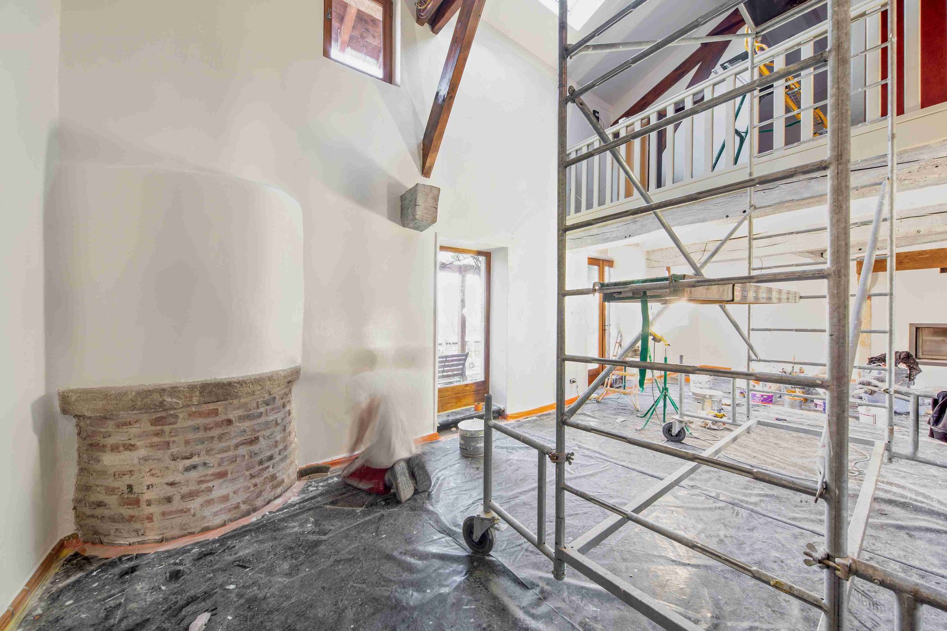 Échafaudages dans une pièce lumineuse en rénovation, avec cheminée et poutres apparentes