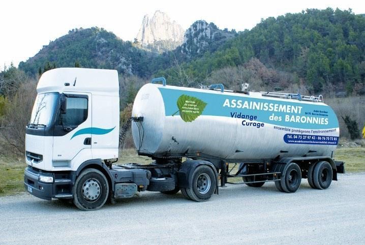 Camion-citerne blanc orné de graphismes bleus et verts, stationné sur une route avec des montagnes en arrière-plan.