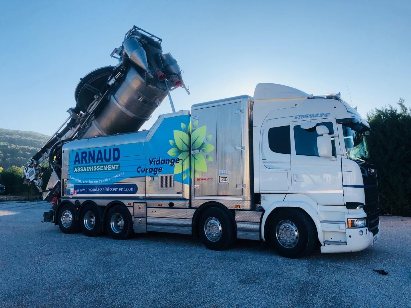 Camion blanc équipé d'un gros aspirateur, stationné à l'extérieur.