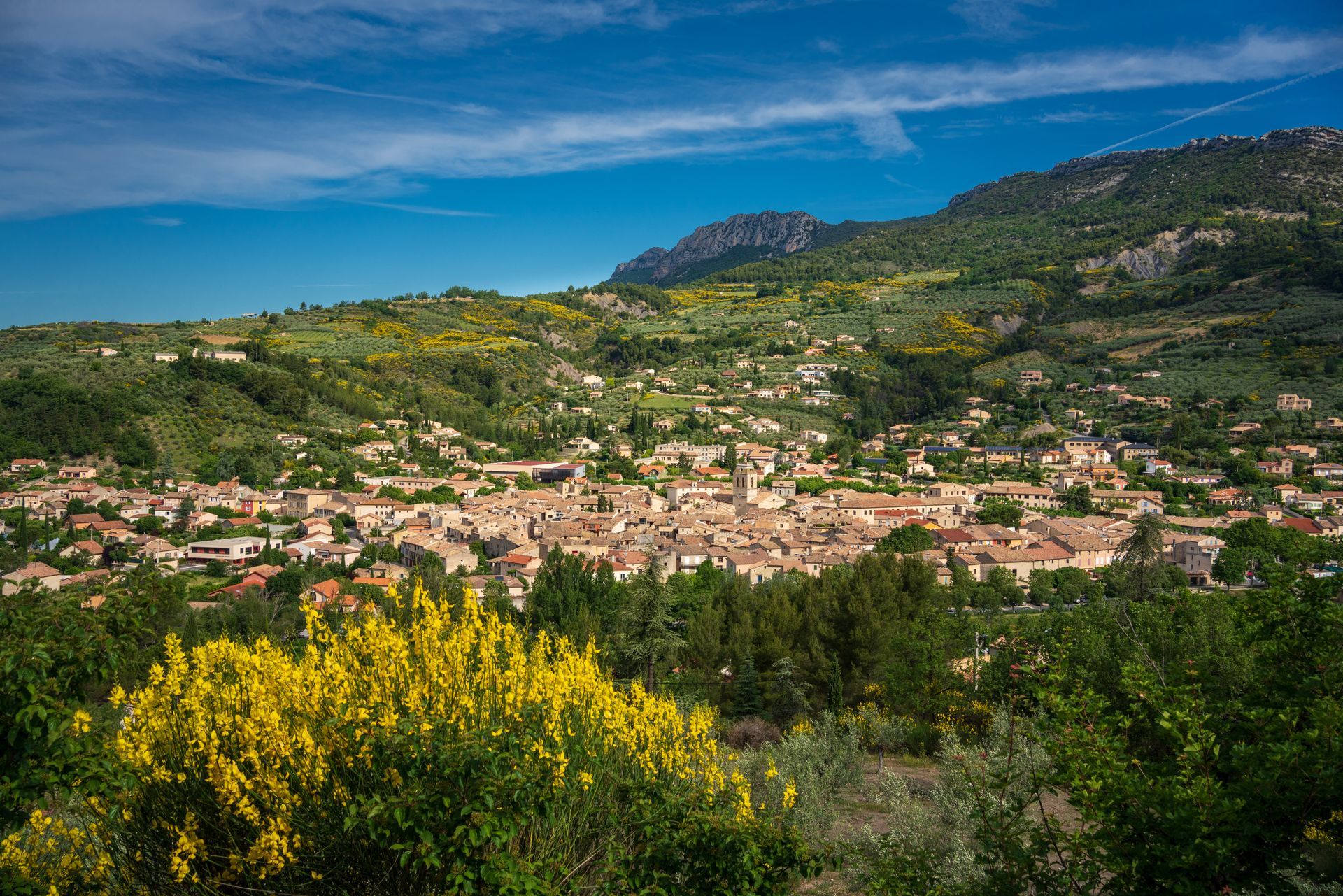 Vue ensoleillée d'une petite ville européenne nichée dans une vallée verdoyante, avec les montagnes en arrière-plan.