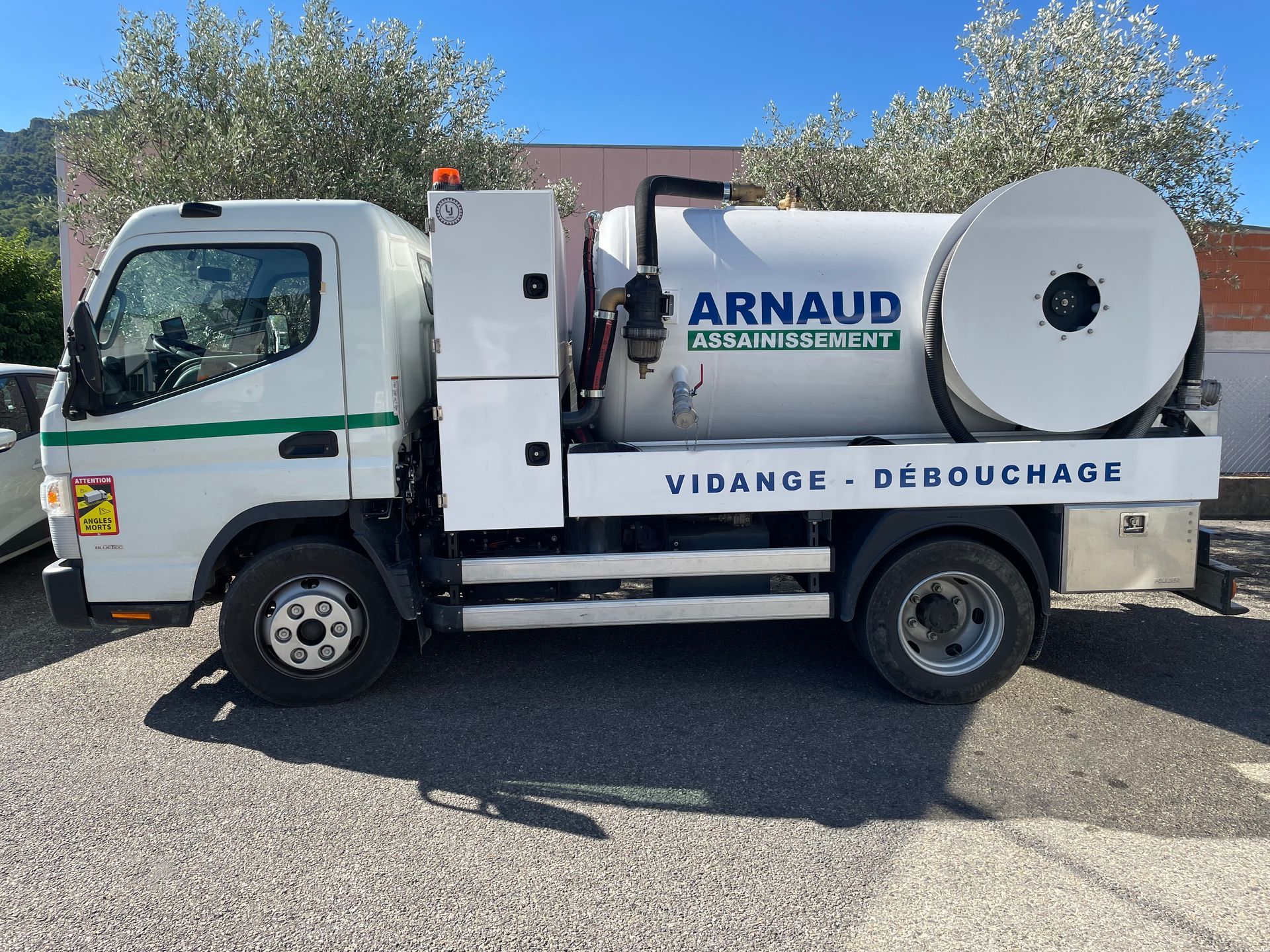 Camion de travail blanc avec réservoir et bobine, en extérieur par une journée ensoleillée.