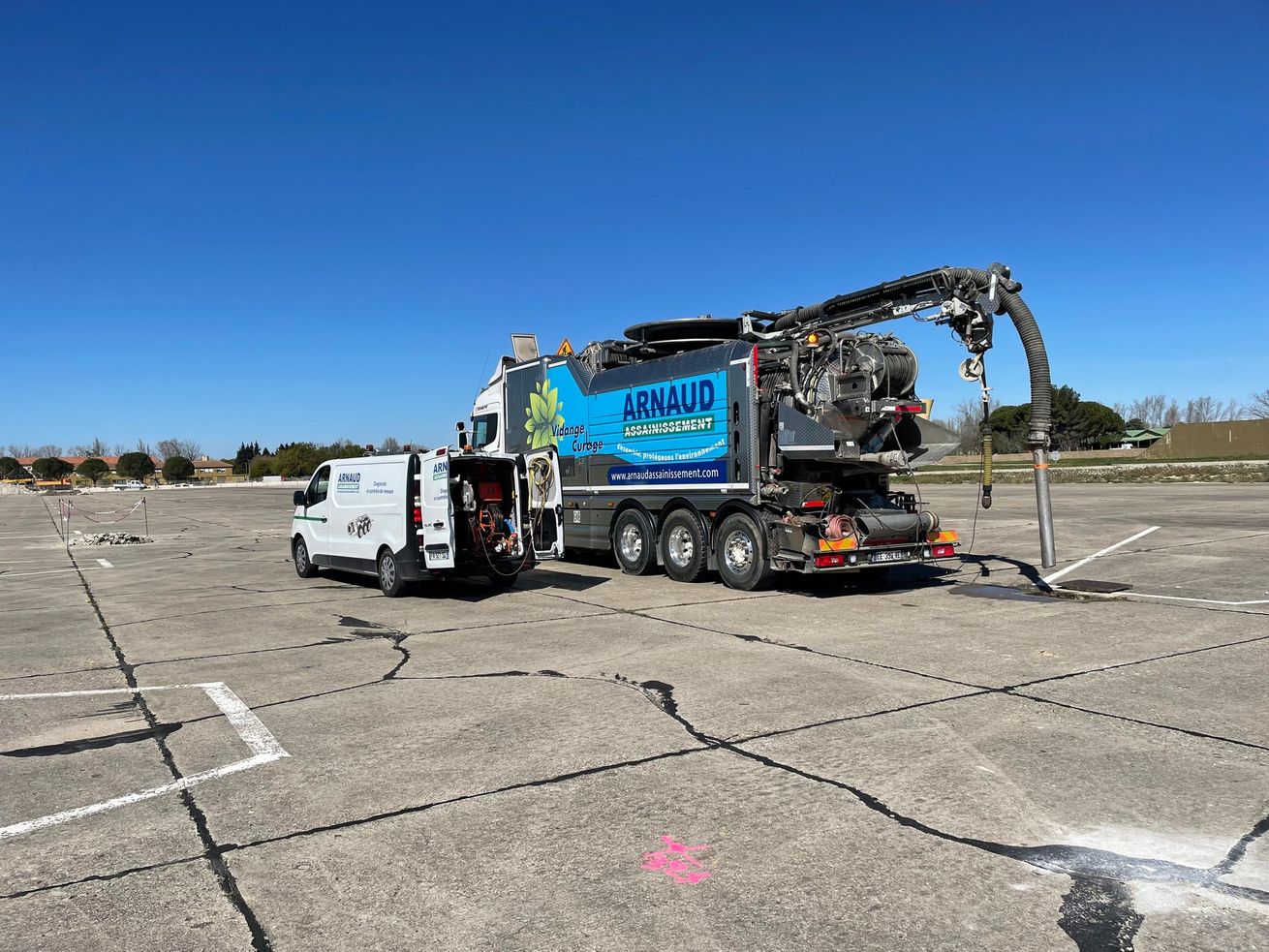 Camion blanc stationné sur une pelouse près d'une montagne. Arbres aux feuilles jaunes au premier plan. Ciel bleu.