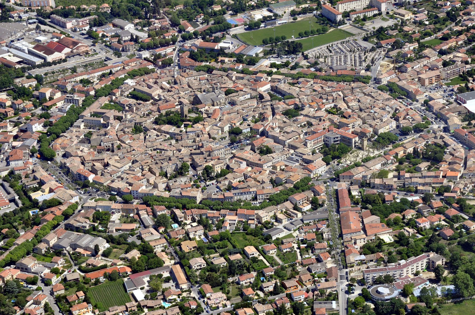 Vue aérienne d'une ville médiévale fortifiée de forme ovale, entourée de bâtiments modernes et d'arbres.