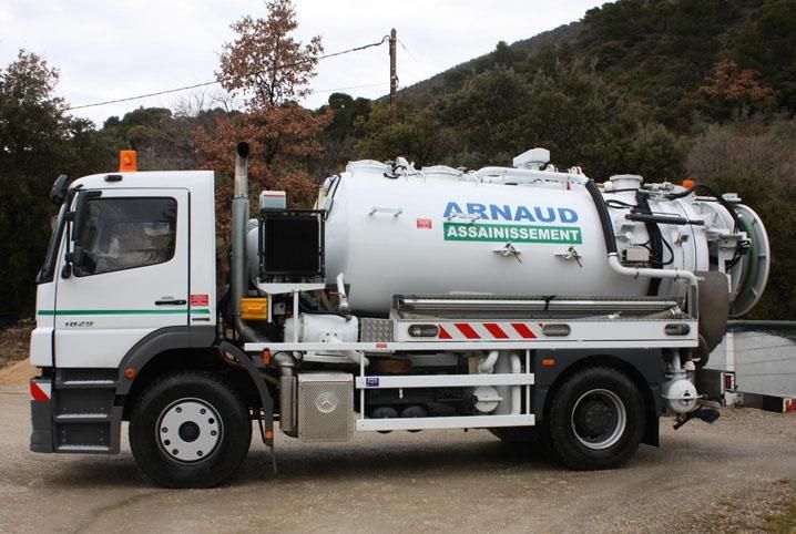 Camion de ramassage blanc portant le logo « ASSASSINAT D'ARNAUD ». Stationné à l'extérieur, près d'arbres.