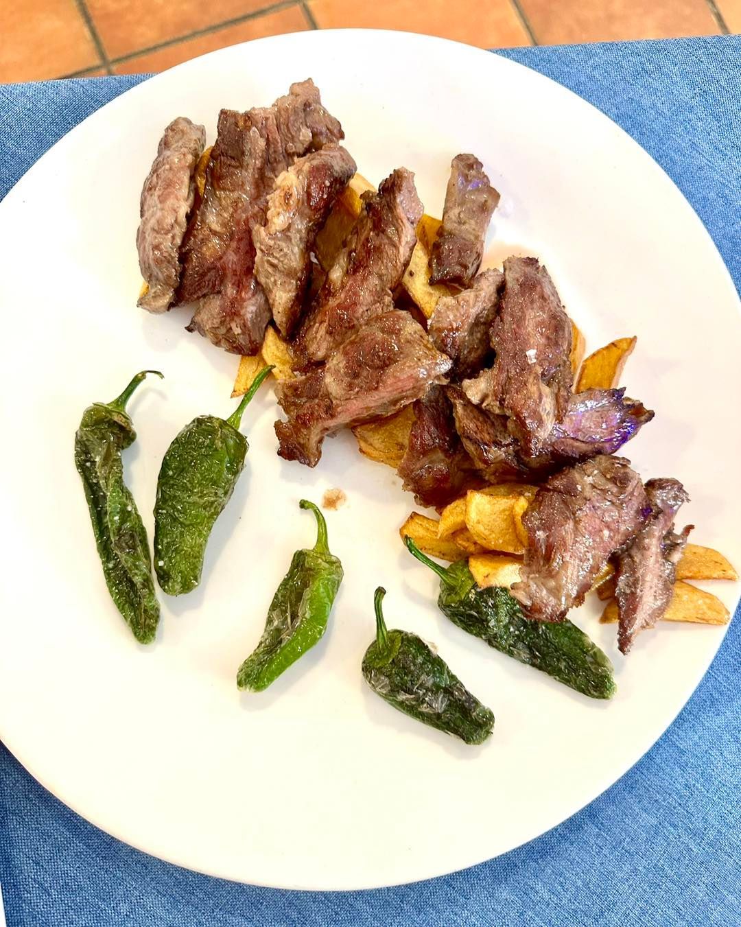 Filete a la parrilla en rodajas y patatas fritas con pimientos verdes en un plato blanco.