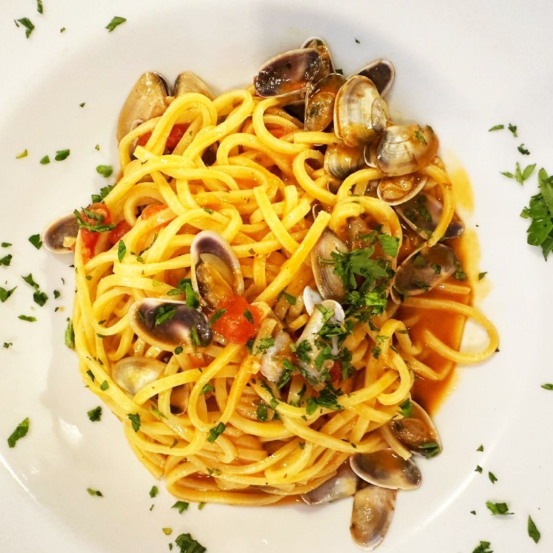 Linguine con almejas y salsa de tomate, adornado con perejil, servido en un plato blanco.