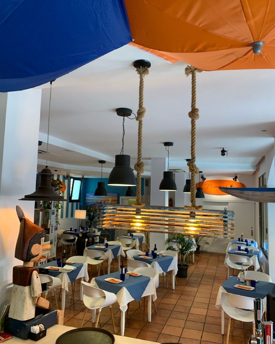 Interior de restaurante con mesas preparadas para cenar, decoración de techo azul y naranja e iluminación de temática náutica.