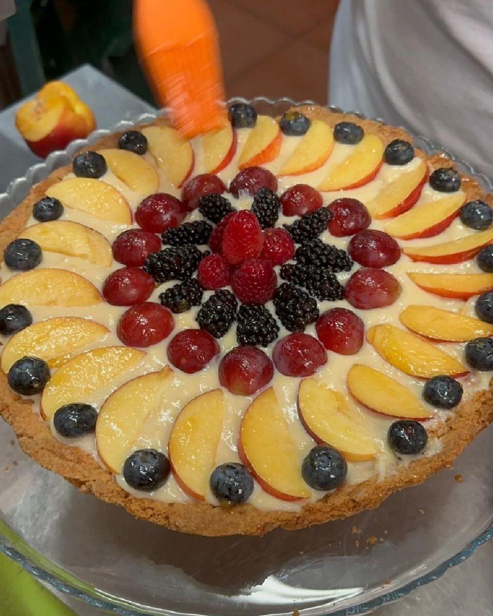 Tarta de frutas decorada con melocotones, arándanos, uvas, frambuesas y moras en un molde de vidrio.