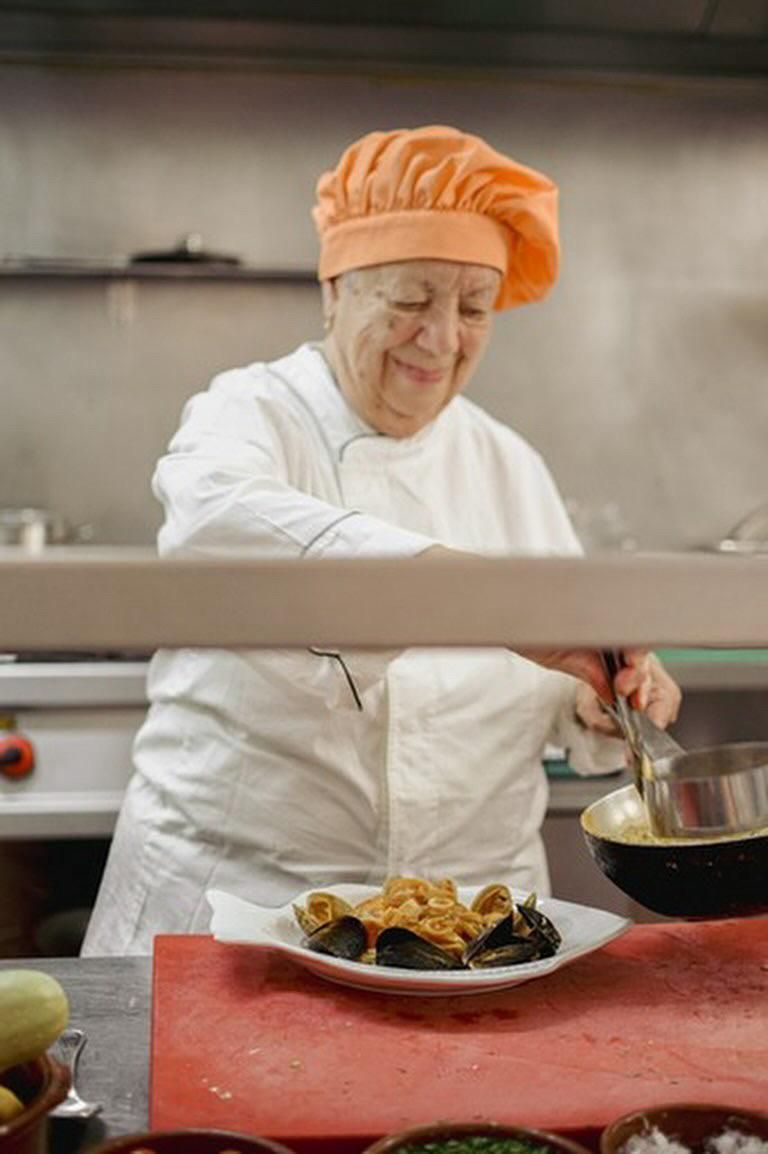 Chef con sombrero naranja y uniforme blanco, emplatando comida en una cocina.