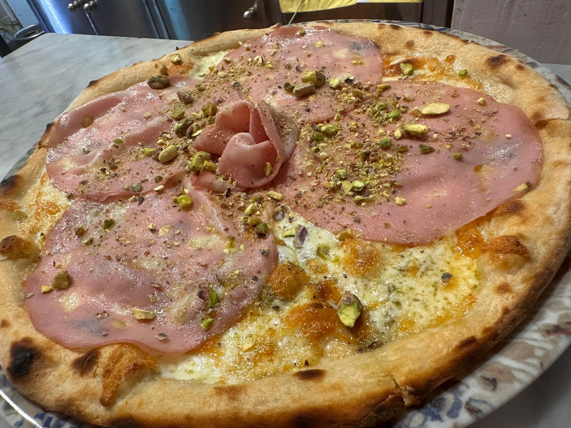 Personas compartiendo una pizza con prosciutto, rúcula y tomate en un plato en una mesa. Una persona sostiene una rebanada.