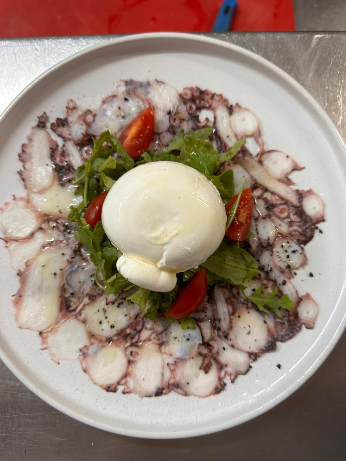 Carpaccio de pulpo con burrata, rúcula y tomates en un plato blanco.