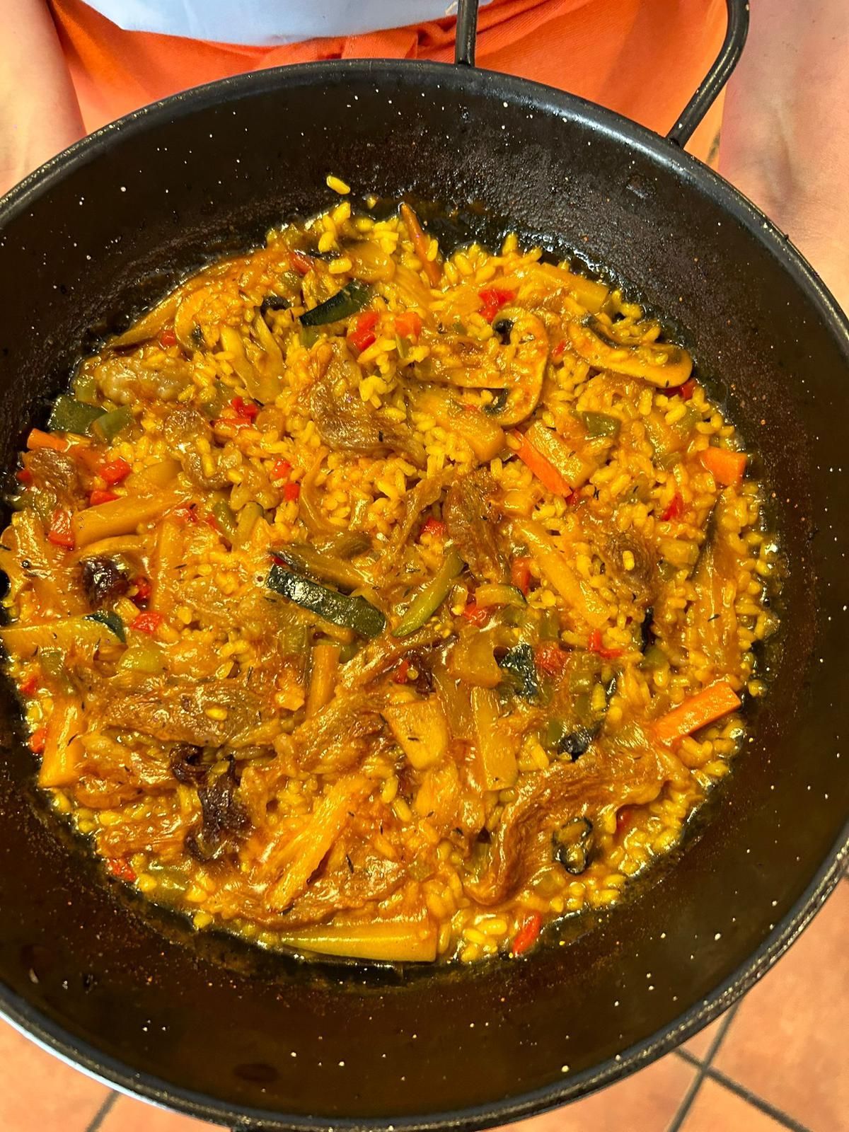 Paella con arroz, verduras y carne en sartén negra; fotografía cenital.