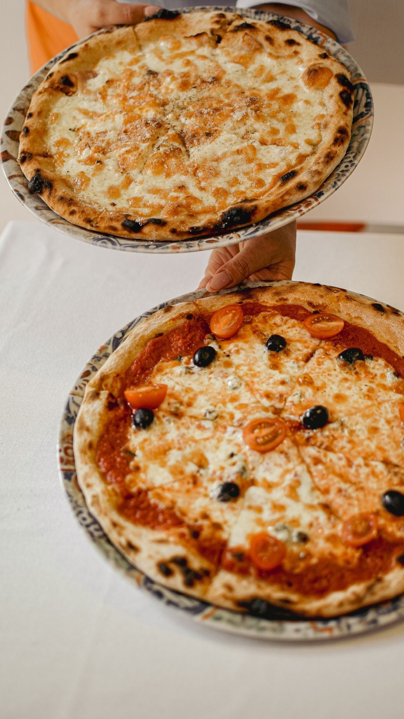 Manos desgarrando una pizza con la corteza burbujeante. Chefs con batas blancas se reúnen alrededor de la pizza.