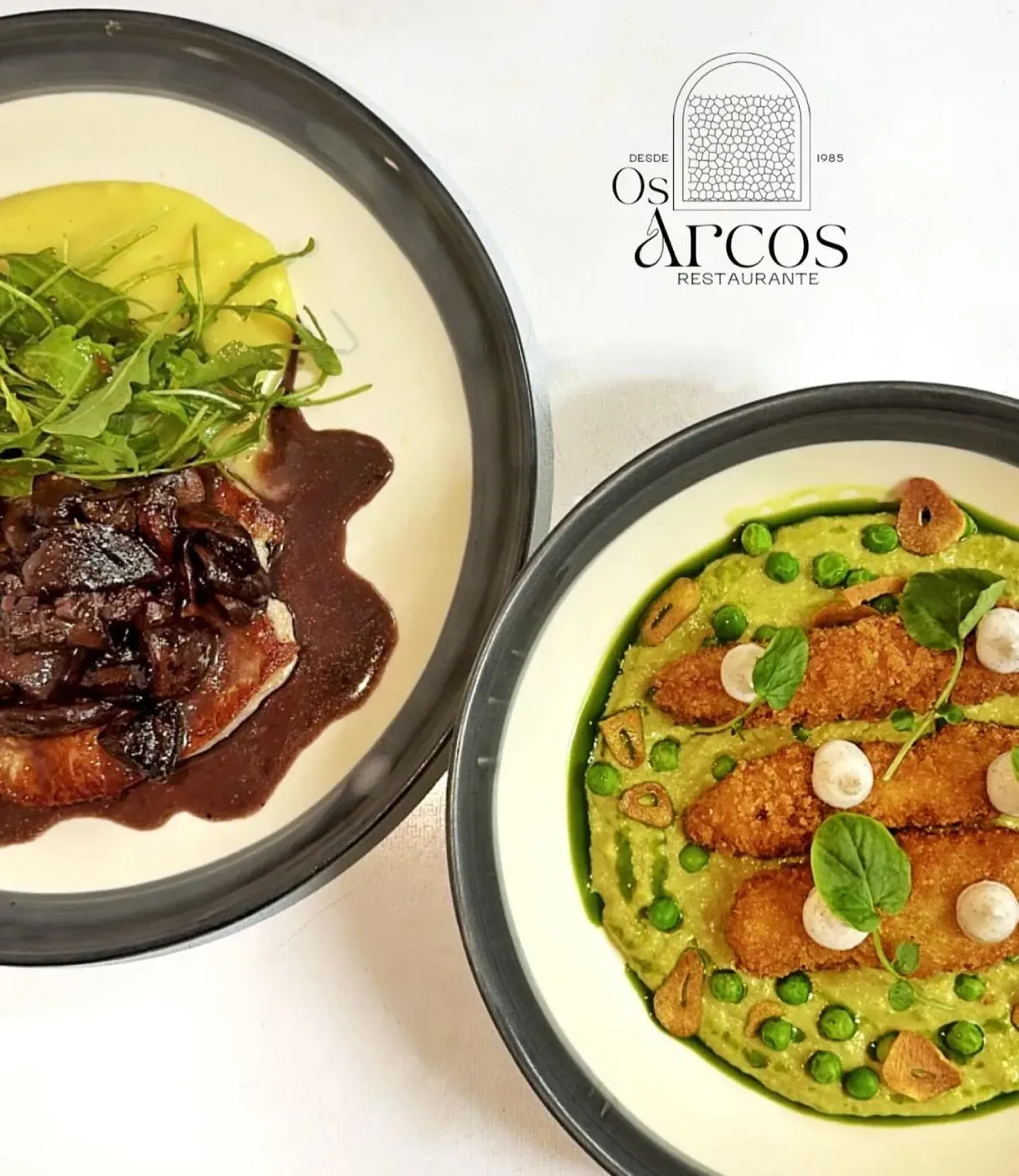 Dos platos de comida con el restaurante Os Arcos al fondo.