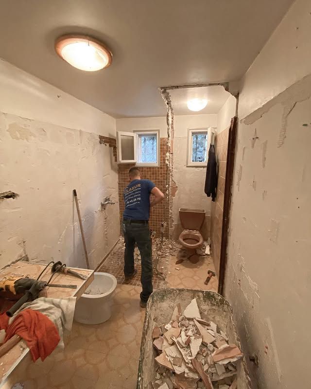 Une personne démolit un mur de salle de bain, des débris dans une brouette.