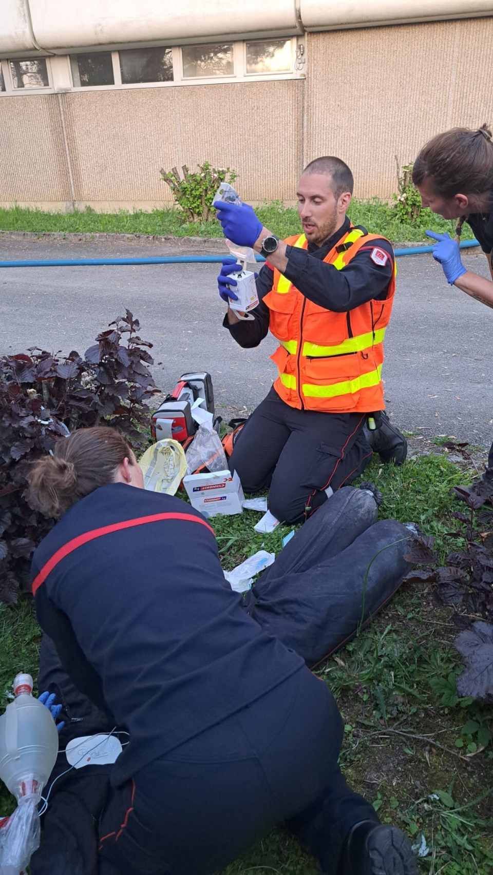 Trois personnes en tenue de secours examinent du matériel près de la végétation.