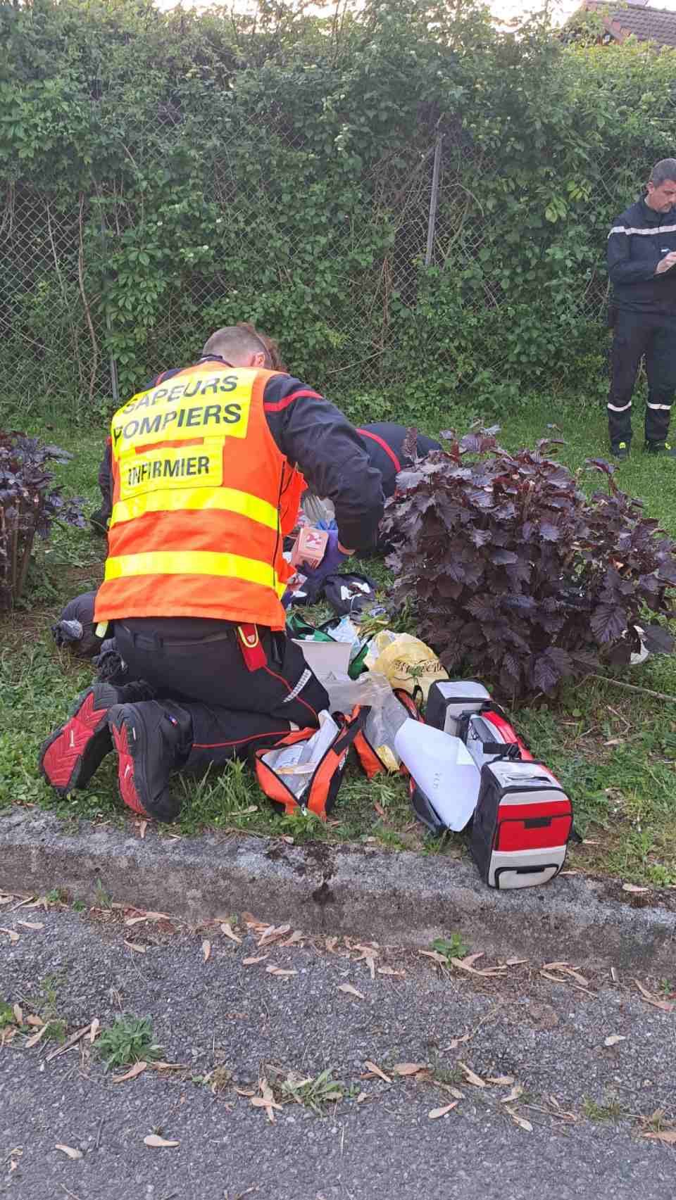Un secouriste s'agenouille et porte assistance à une personne à côté d'un équipement médical installé sur l'herbe ; un autre secouriste se trouve à proximité.