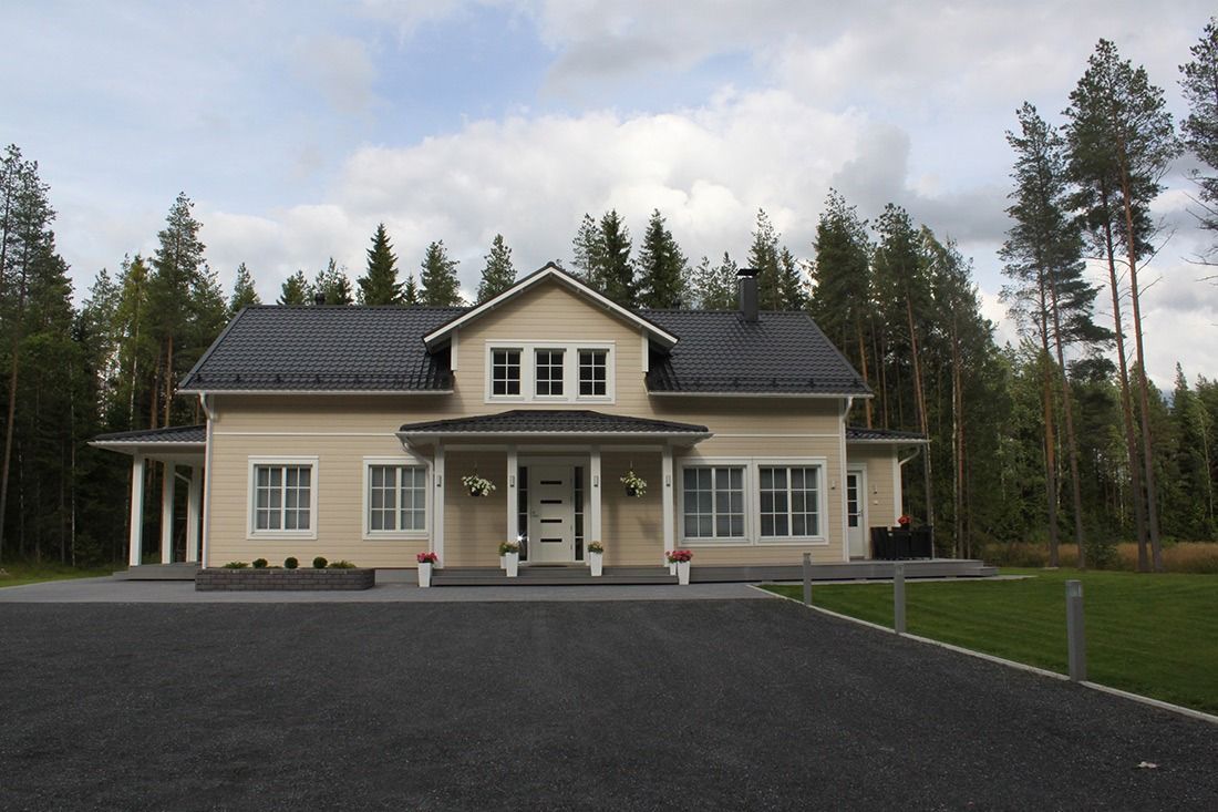 Beige talo, jossa on musta katto, kuisti ja puiden ympäröimä soratie