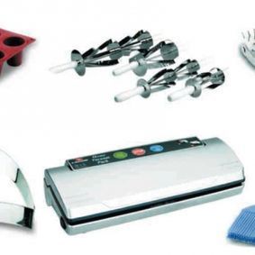 Una selladora al vacío está rodeada de varios utensilios de cocina.