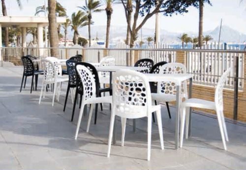 Una fila de mesas y sillas blancas en un patio con palmeras al fondo.