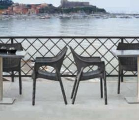 Dos sillas y dos mesas están sentadas en un balcón con vista al océano.