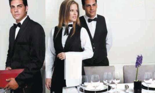 Dos camareros y una camarera están de pie delante de una mesa de restaurante.