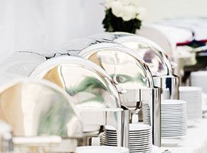 Una línea de buffet con platos y cubiertos sobre una mesa.