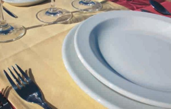 Platos blancos y cubiertos sobre una mesa con copas de vino.