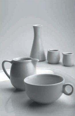 Un grupo de tazas, jarras y azucareros de cerámica blanca sobre una mesa.