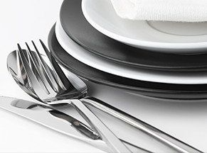 Una pila de platos, cubiertos y una servilleta sobre una mesa.