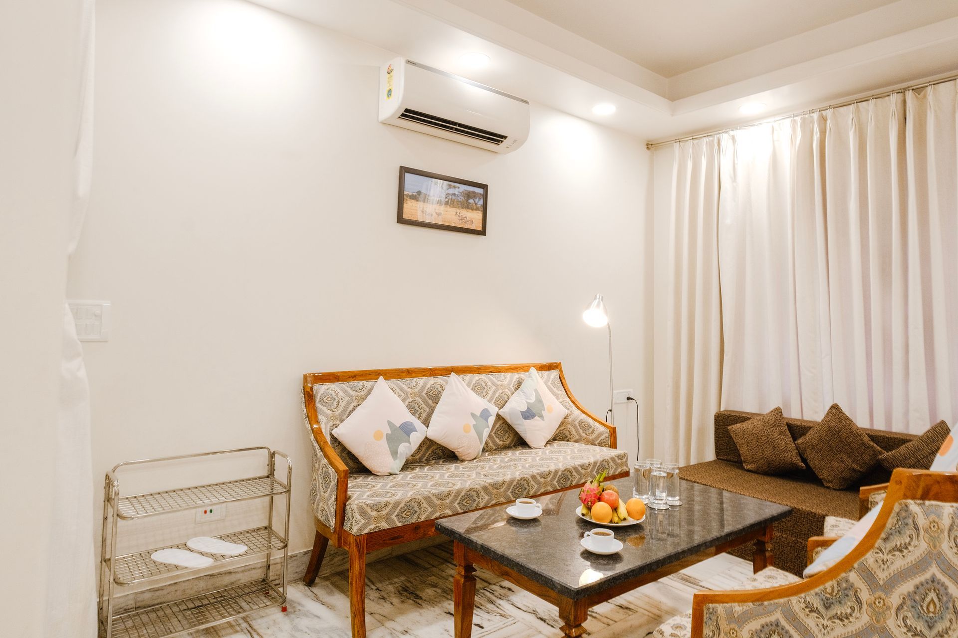 Bright living room with wicker sofa, coffee table, cream curtains, and wall-mounted air conditioner