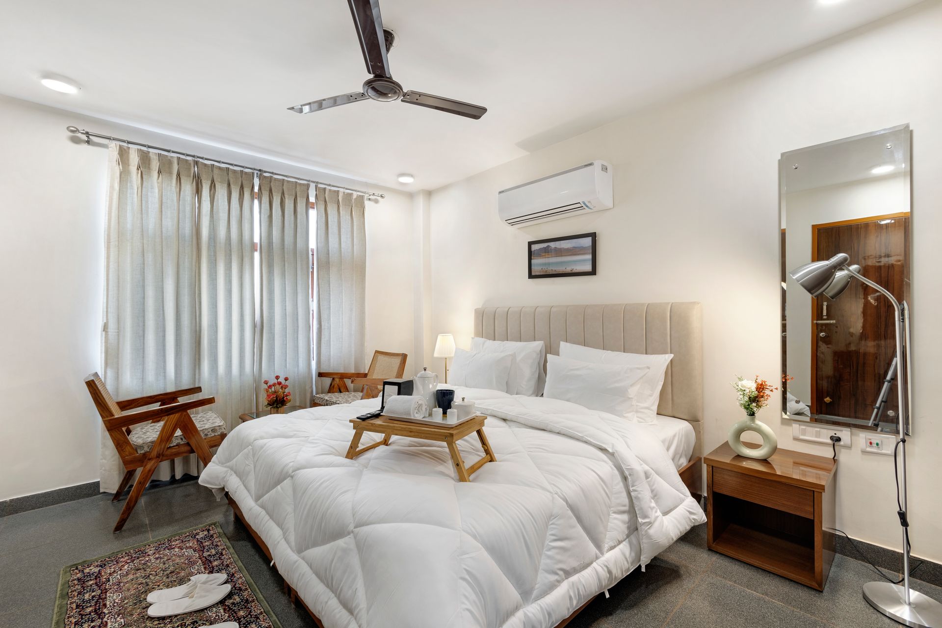 Bright modern bedroom with a white bed, bedside table, mirror, chair, and curtains
