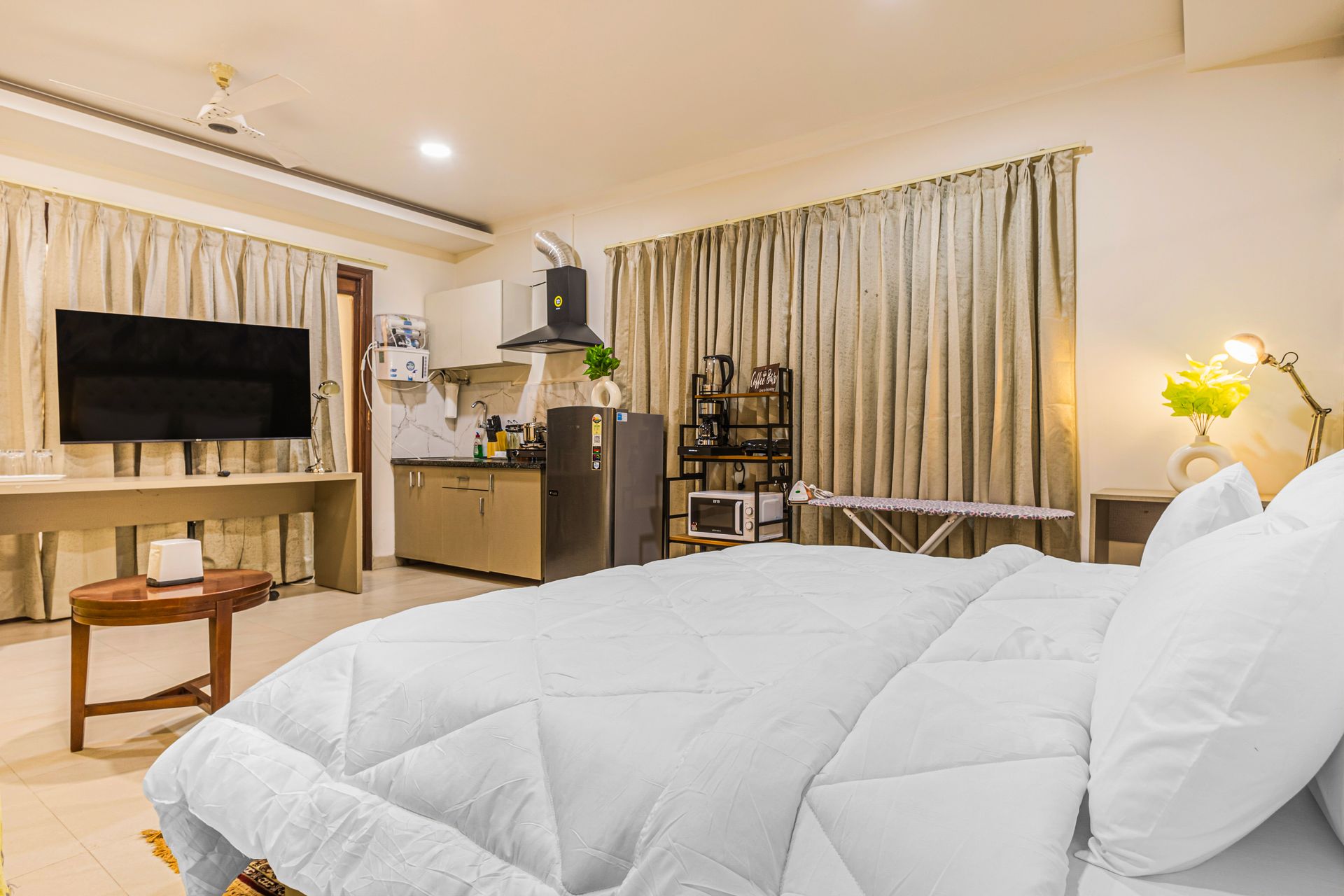Bright modern bedroom with a large white bed, TV, curtains, and warm lamp lighting