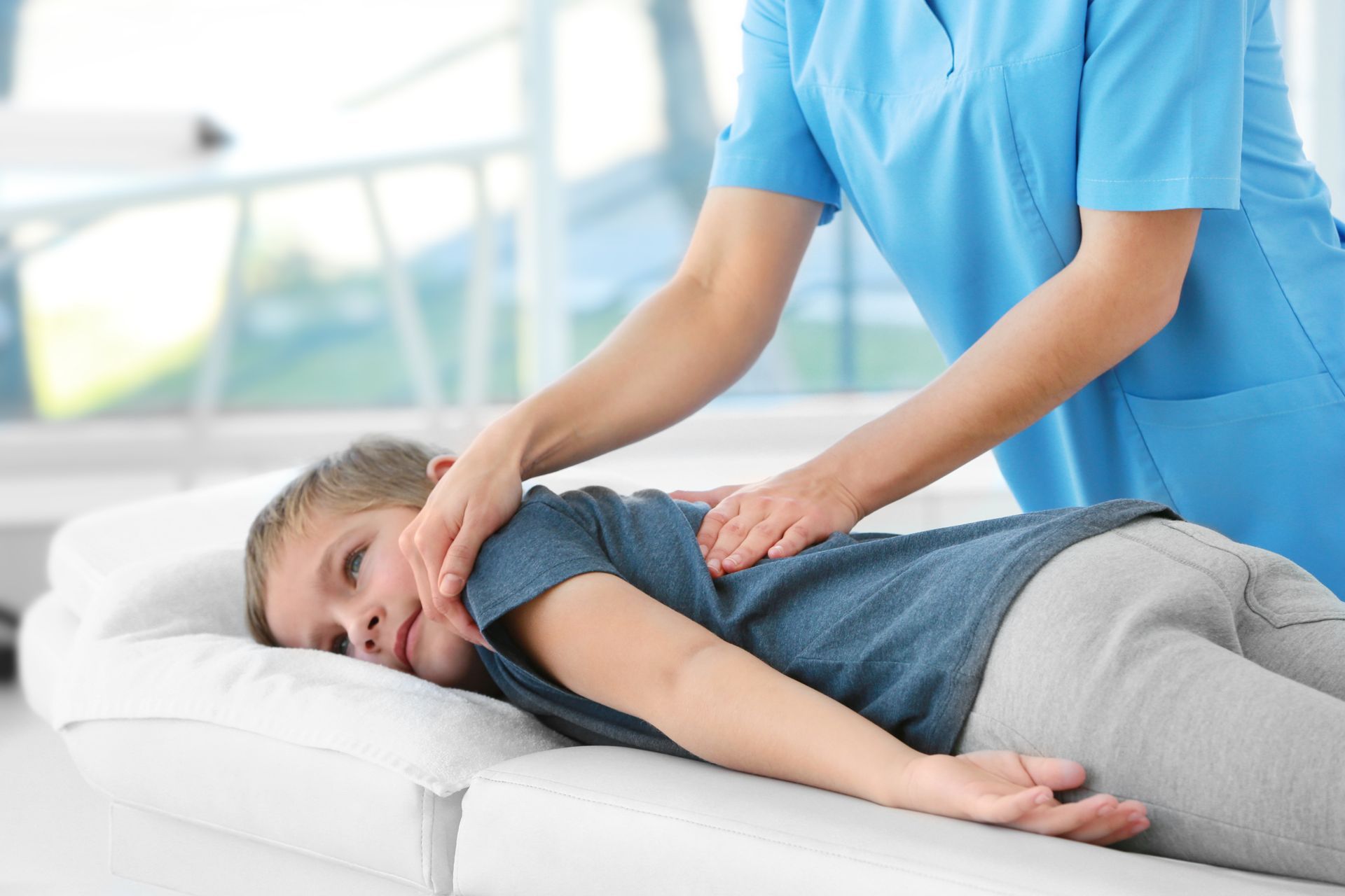 Un thérapeute effectue un massage des épaules sur un patient allongé sur une table de traitement.