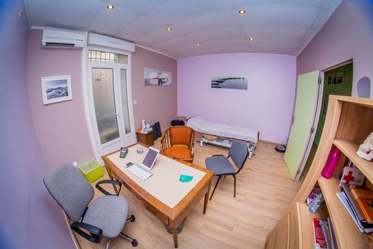 Petite pièce aux murs rose pâle, parquet, lit, bureau, chaise et porte verte ouverte.