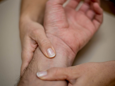 Des mains massent le dos d'une personne allongée sur le ventre sur un drap blanc