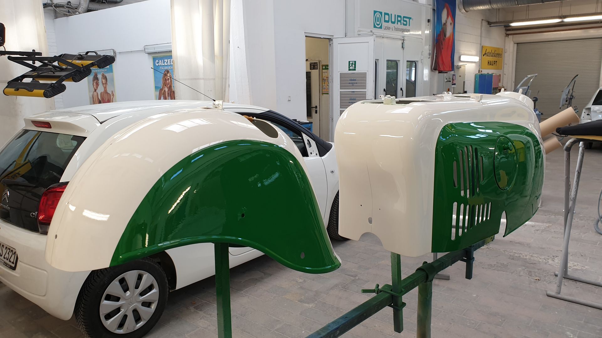 Grüne und weiße Karosserieteile in einer Autowerkstatt mit Geräten im Hintergrund
