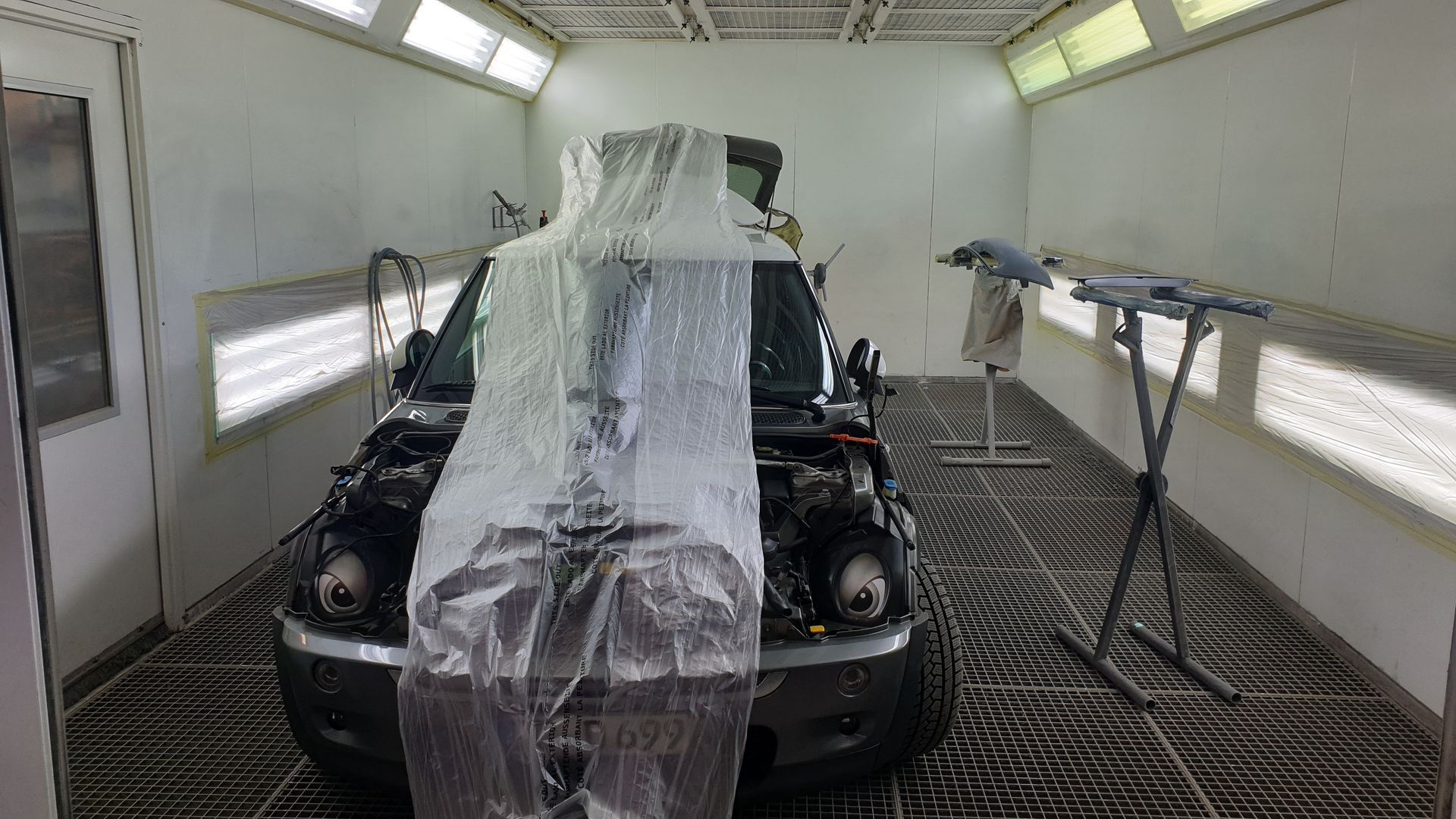 Das Auto steht in einer Lackierkabine, ist mit Plastikfolie abgedeckt und für die Spritzlackierung abgeklebt.