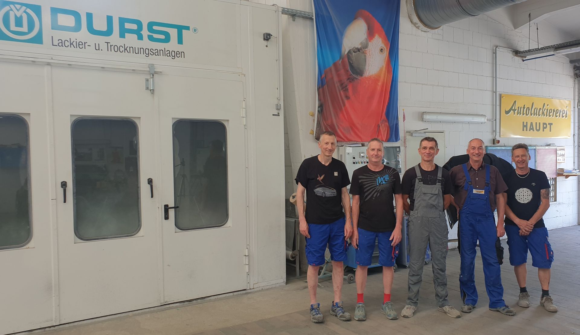 Fünf Personen stehen in einer Werkstatt vor einer großen blau-weißen Durst-Industriemaschine.