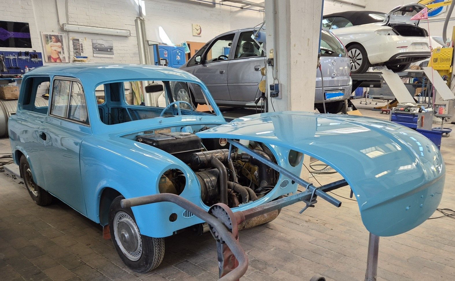 Blauer Oldtimer mit abmontierter Frontpartie in einer Autowerkstatt, Motor freigelegt, Motorhaube abgenommen in der Nähe